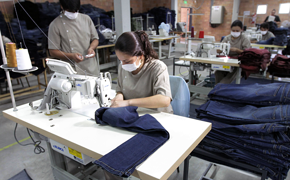 Costureras trabajando con máquinas de coser, cubiertas con tapabocas, en una fábrica textil.