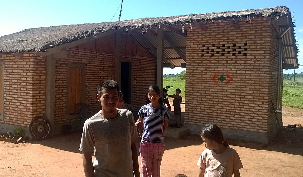 Familia de indígenas frente a su vivienda.
