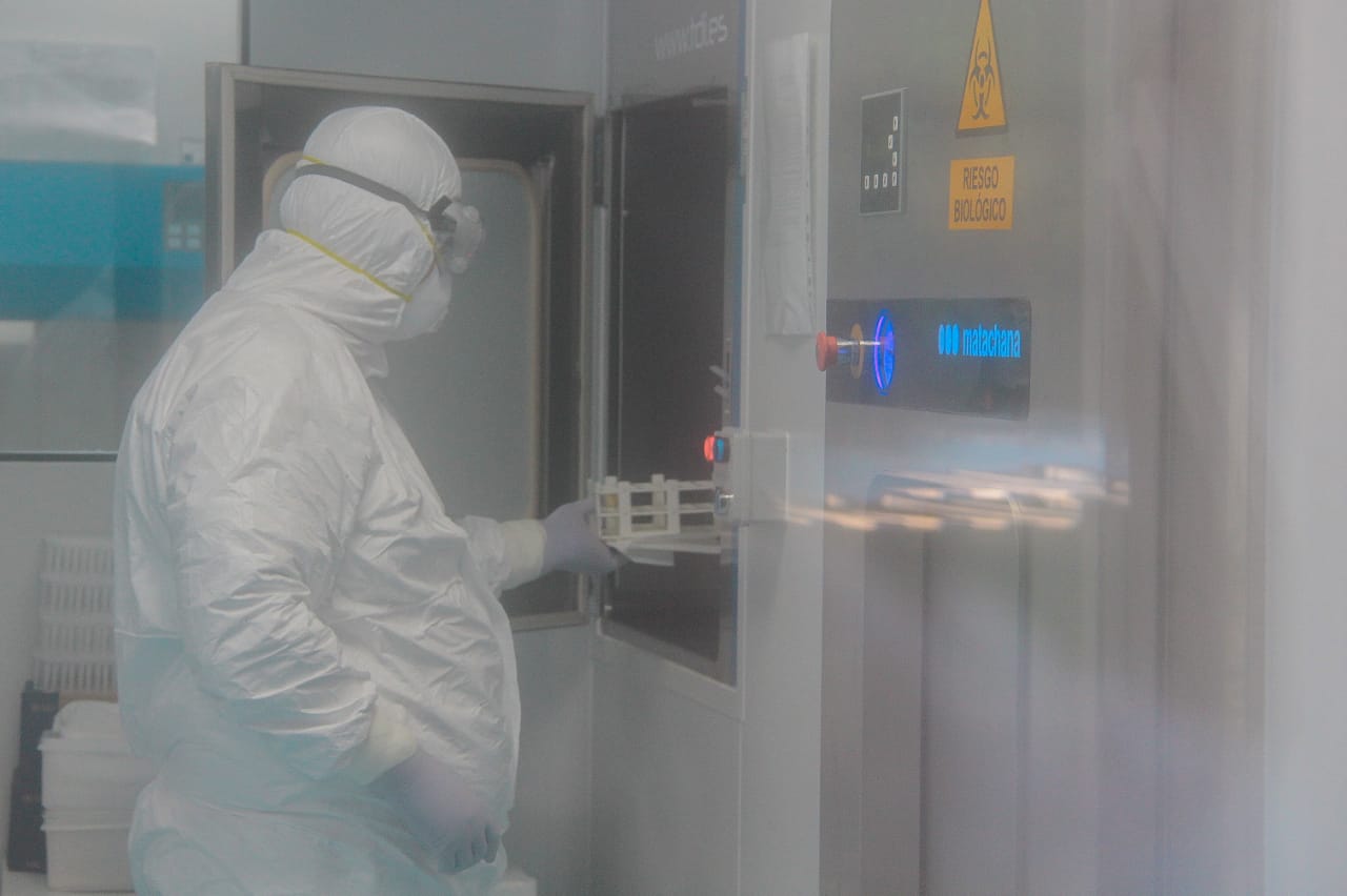 Profesional trabajando en un laboratorio con muestras de Covid-19, vestido con el equipo completo de bioseguridad.