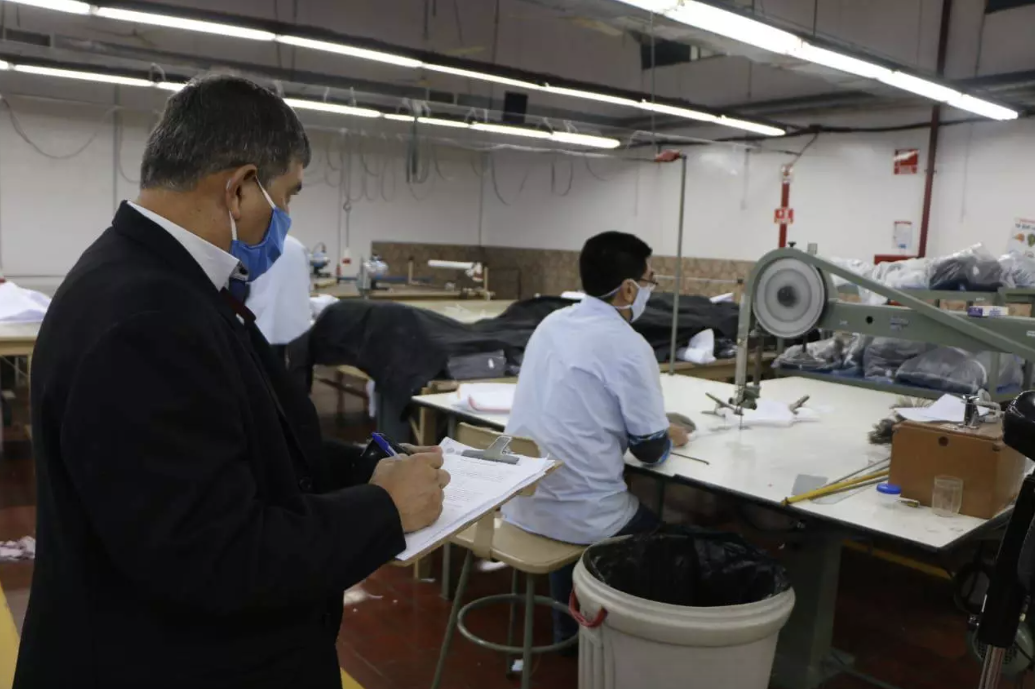 Trabajador textil en su puesto de trabajo, y un supervisor controlando.