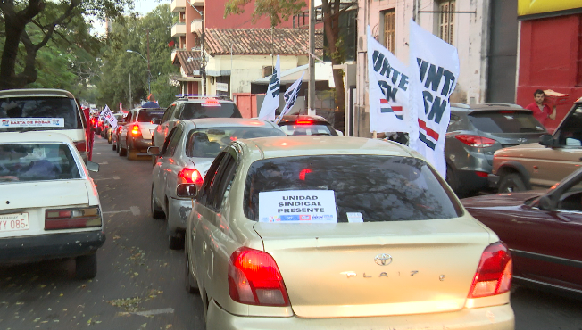 Caravana de autos manifestándose con banderas y carteles.