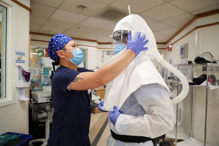 Médico ayudando a otro médico a ponerse el traje de protección