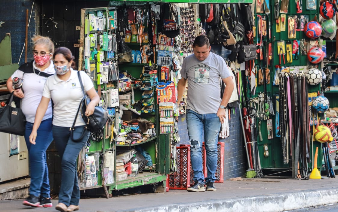 Un hombre sin tapabocas en su negocio del mercado 4, y dos mujeres pasan caminando con tapabocas.