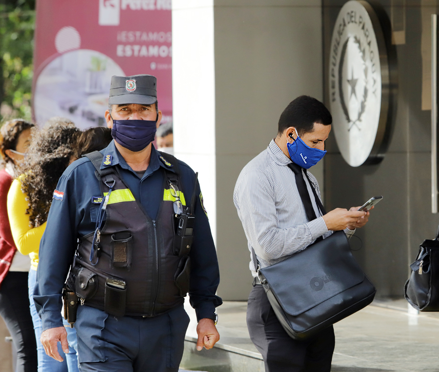 Policía vistiendo una mascarilla, cuidando la seguridad en las afueras de una institución pública.