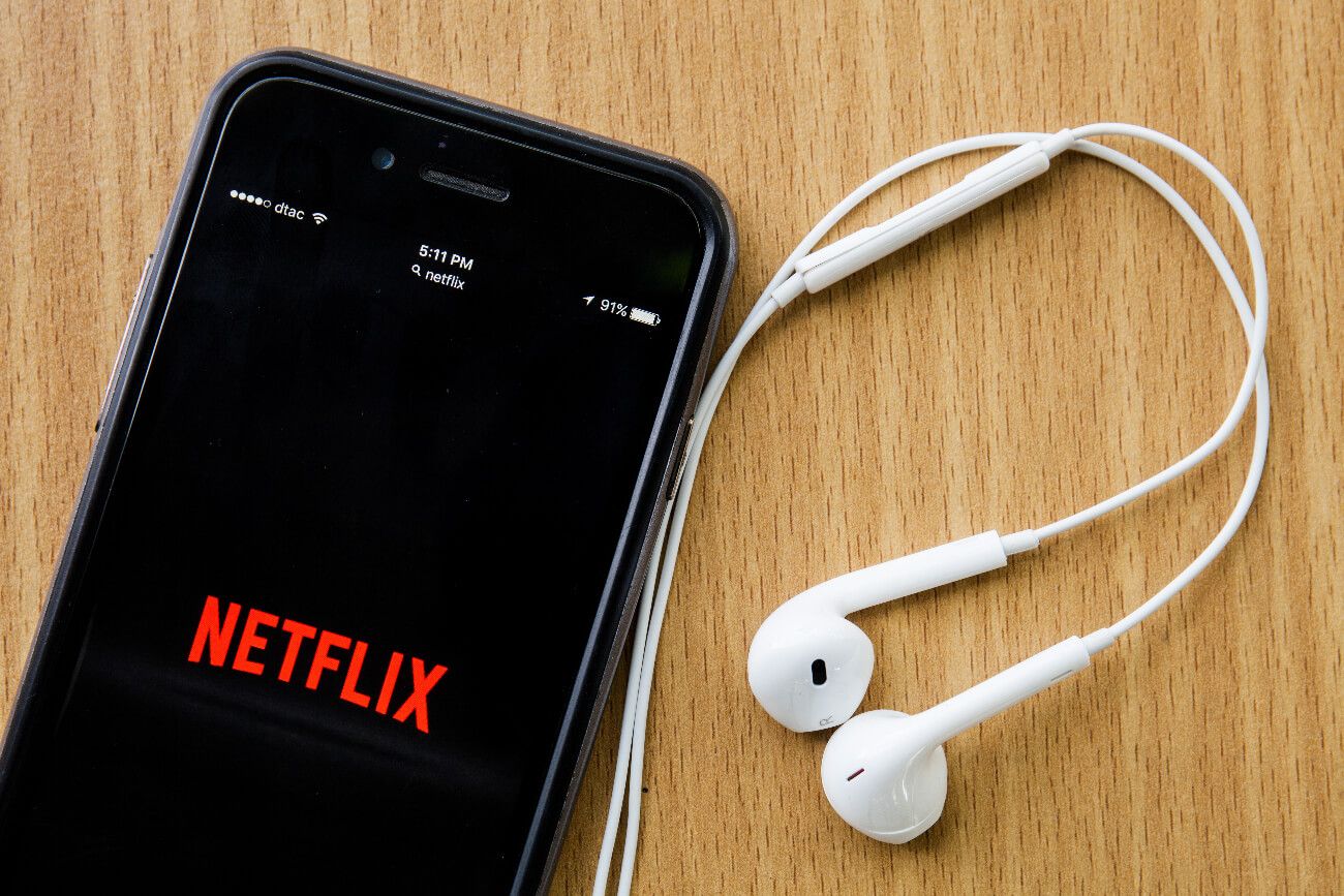 Imagen ilustrativa. Aplicación de Netflix iniciándose en un teléfono celular, junto con unos auriculares.