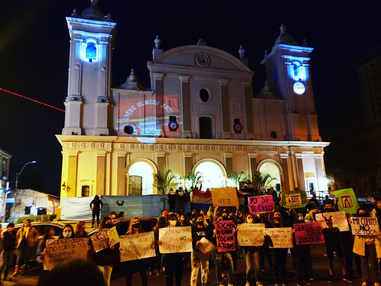 Grupo de manifestantes, frente a la Catedral de Asunción, con carteles y proyecciones en repudio de la justicia paraguaya y el cura Silvestre Olmedo.