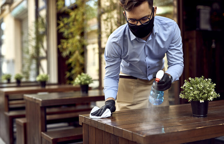 Empleado limpiando una mesa de restaurante, usando mascarilla y guantes.