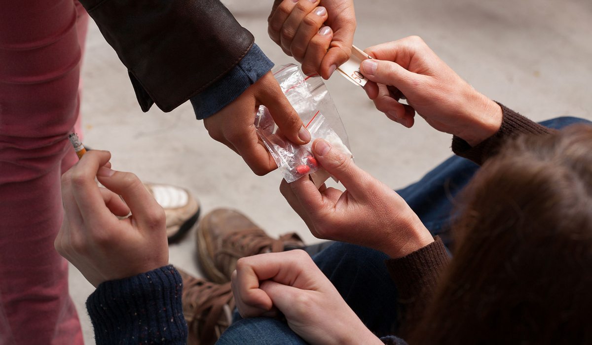 Imagen ilustrativa de manos de jóvenes pasándose sobres de drogas.